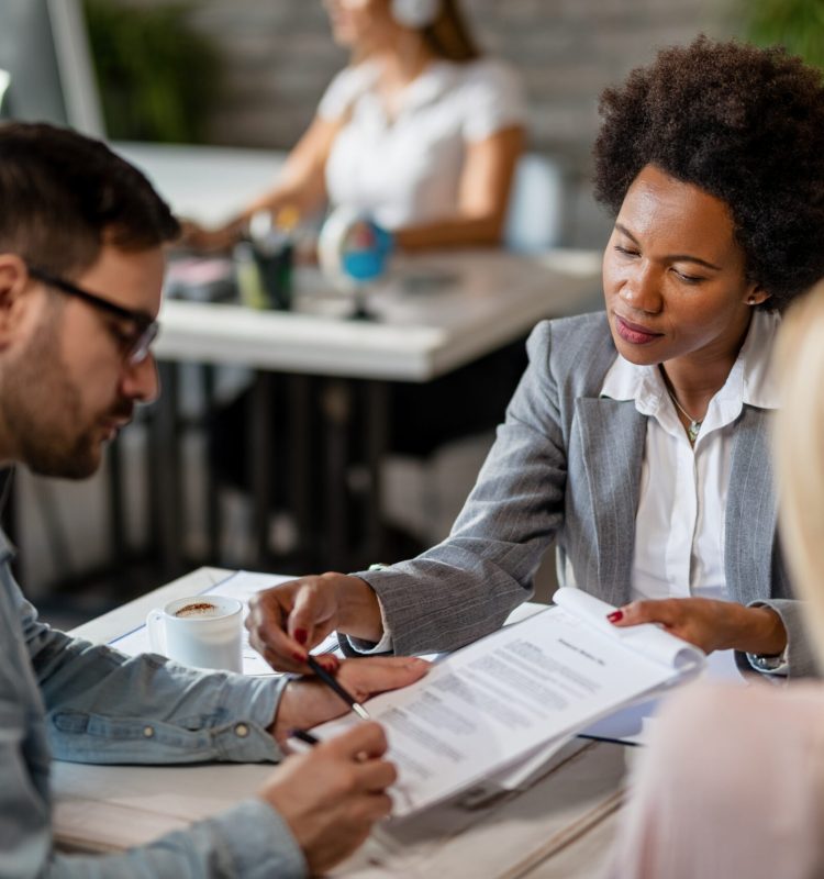 Black female real estate agent showing to a couple where to sign the contract during the meeting in the office.