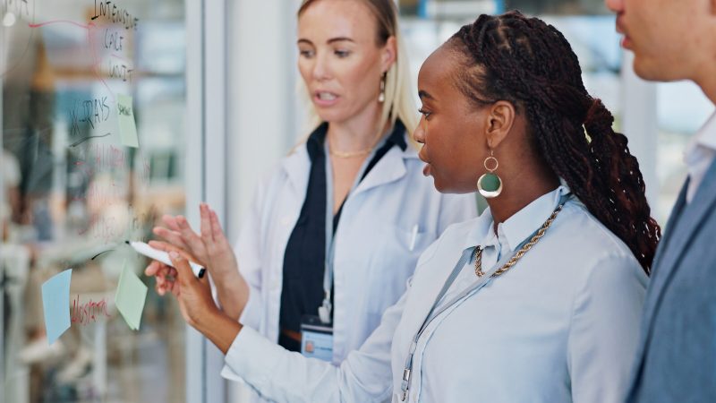 Doctors, solution and writing on glass for healthcare research, brainstorming and problem solving with notes. Professional leader, executive or medical team with planning, interns or ideas for clinic.